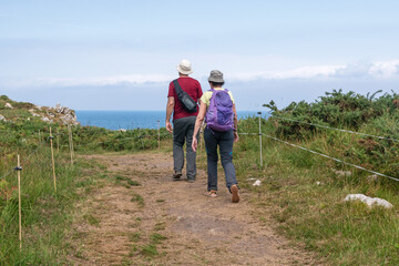 Fototapeta na wymiar Adult couple walking along the coast with hats. Summer in Asturias