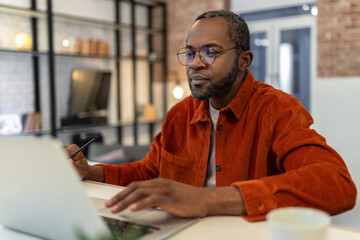 Dark-skinned man in red shirt working at home and looking involved