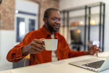 Dark-skinned man in red shirt working at home and having coffee