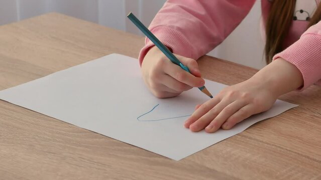 A small preschool child draws on a piece of paper with a pencil with a convenient silicone pencil attachment. The correct grip of the pencil.