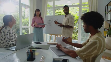 Medium long shot of diverse coworkers standing near whiteboard with app design having meeting with team in office - Powered by Adobe