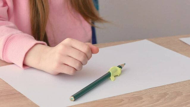 A small preschool child draws on a piece of paper with a pencil with a convenient silicone pencil attachment. He put the pencil on the table.