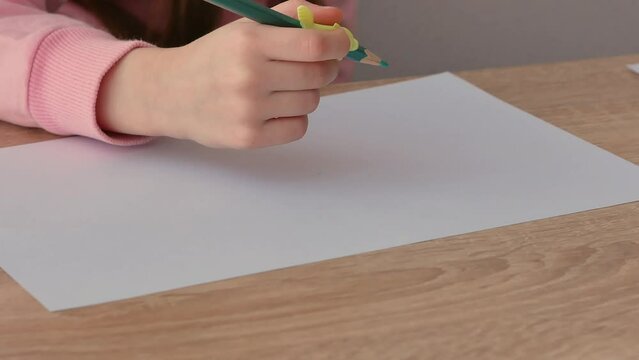 A child's hand holding a pencil with a silicone pencil attachment draws on paper when it is not properly gripped. The development of children, teach them to hold a pen.