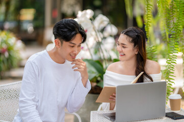 Two colleagues share a light-hearted moment while discussing work, with a laptop, in a verdant outdoor café setting.
