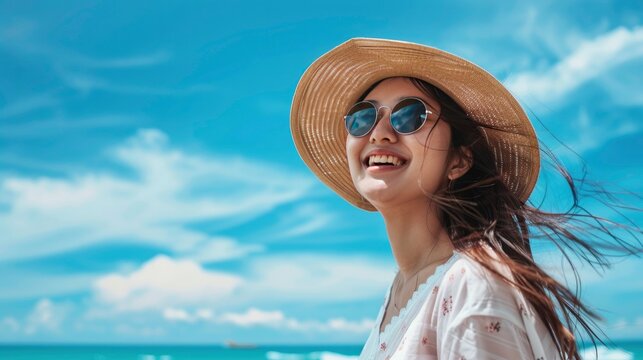 A beautiful woman wearing sunglasses and a hat on the beach, with a blue sky background.