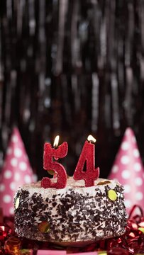 Number fifty-four birthday candle on sweet cake on dark background, 54th birthday. Blow out the holiday candle.