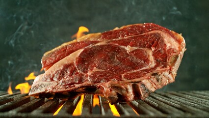Close-up of tasty raw beef steak on cast-iron grate with fire flames - 768735720