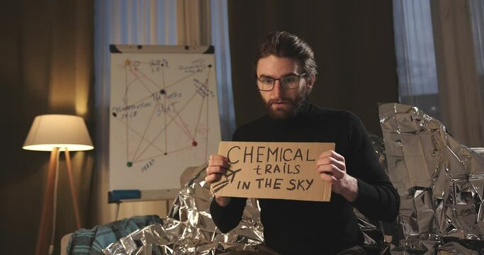 A paranoid, a supporter of pseudoscience holds a sign with a conspiracy slogan.