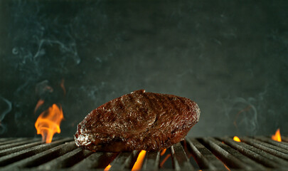 Close-up of tasty raw beef steak on cast-iron grate with fire flames - 768735997