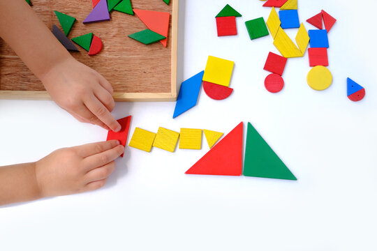 smart little child, girl 3 years old playing with educational toy, wooden geometric figures, wooden puzzles, children's hands create pictures from colored wooden geometric shapes