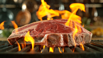 Close-up of tasty raw beef steak on cast-iron grate with fire flames - 768736963