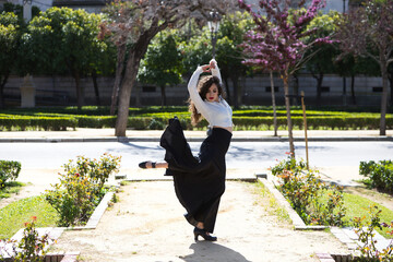 Beautiful woman with long curly hair, dancing flamenco artfully in a park in Seville, Spain....