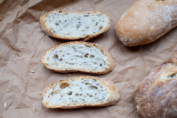 Two baguettes and three slices on a background of kraft parchment. French bread. View from above. Bread on a board.