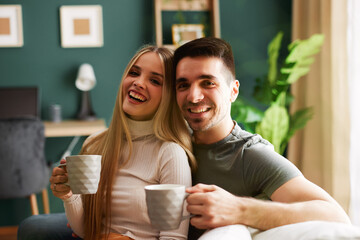 Beautiful young happy couple enjoying coffee at home on sofa