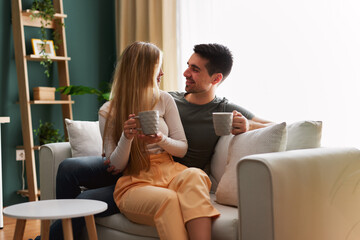 Beautiful young happy couple enjoying coffee at home on sofa - 768742953