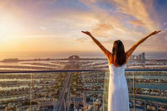 A happy woman looks at the panoramic view of the Pam Dubai  district during golden sunset time, UAE