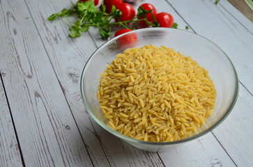 Raw pasta Orzo in glass bowl on wooden background. Top view, copy space