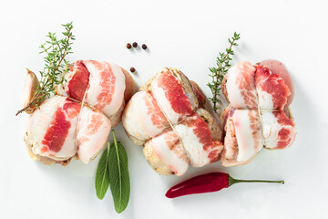 uncooked chicken thighs wrapped in bacon. Italian cuisine. on white - obrazy, fototapety, plakaty