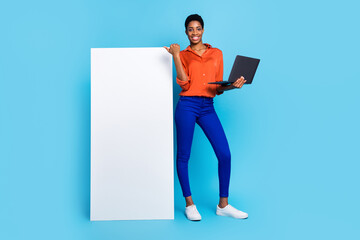 Photo of lady hold netbook direct thumb white vertical empty space poster wear brown shirt isolated blue color background - obrazy, fototapety, plakaty