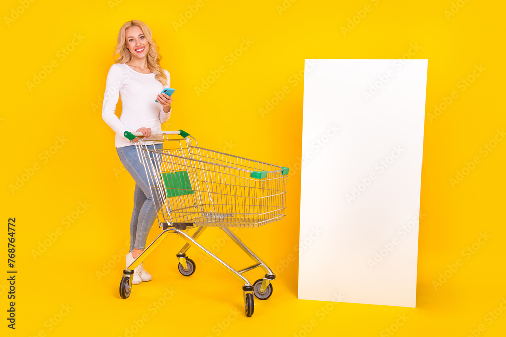 Poster Full length photo of pretty young blond lady do shopping hold telephone wear shirt jeans sneakers isolated on yellow background