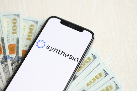 KYIV, UKRAINE - MARCH 17, 2024 Synthesia logo on iPhone display screen with many hundred dollar bills. Artificial Intelligence engine