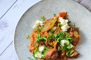 Rice with lamb meat and vegetables on a plate on a wooden table