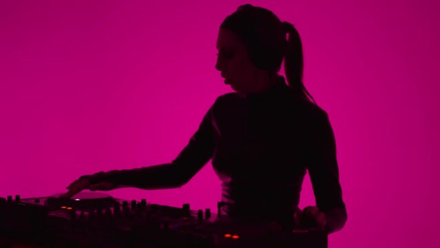 Woman DJ In Headphones Mixing Tracks Of Modern Electronic Music, Portrait In Pink Background
