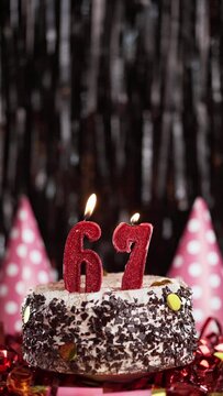 Number sixty-seven birthday candle on sweet cake on dark background, 67th birthday. Blow out the holiday candle.