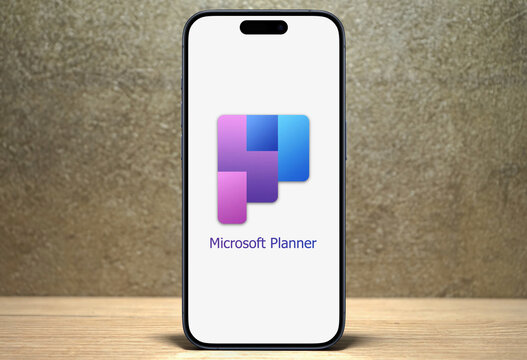 2024 Microsoft Planner logo is displayed on a modern smartphone standing on a wooden desk, planning application available on the Microsoft 365 platform, team management, file sharing, and organization