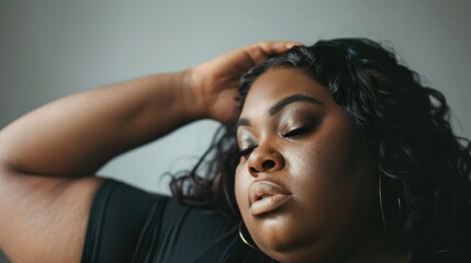 Fototapeta premium A woman with closed eyes resting her head on her hand wearing a black top and gold hoop earrings with her dark curly hair cascading down her shoulders.