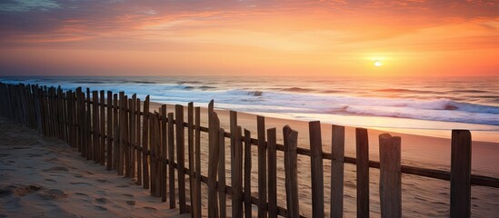 Obraz premium Wooden fence stretching along the sandy beach as the sun sets over the tranquil ocean