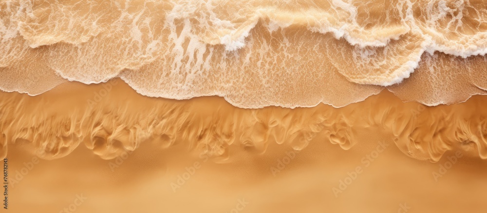 Poster view from above of a beach with sand as the background and a wave rolling towards the shore