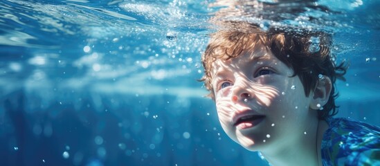 A young boy in a blue shirt is swimming underwater in a pool, surrounded by bubbles while engaging in rehabilitation activities. - obrazy, fototapety, plakaty