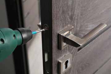Repairing door handle with electric screwdriver indoors, closeup