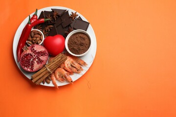 Natural aphrodisiac. Different products and heart model on orange background, top view. Space for...