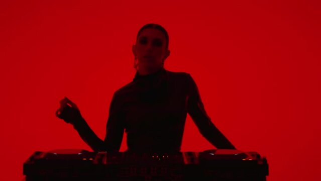 Medium Portrait Shot With Beautiful Female DJ Mixing Tracks In Nightclub Or Studio With Red Lights
