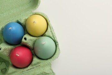 Colorful egg shaped candles in carton on white table, top view. Easter decor