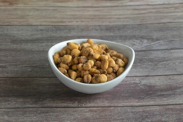 White ceramic bowl filled with salty corn kernels on a wooden tabletop