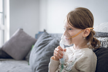 Cute little girl are sitting and holding a nebulizer mask leaning against the face, airway...