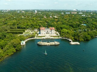 a huge house surrounded by lots of trees and water and an island: The Vizcaya Museum and Gardens