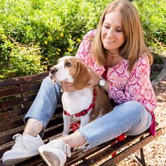 Portrait of beautiful woman sitting on wooden bench with her beagle dog.