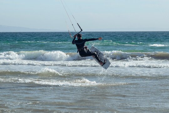 Hispanic young man doing kitesurfing with foamy waves in Tarifa, Spain on a sunny day
