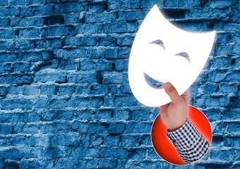Mystery Behind the Mask. Composite Collage. Hand Holding White Smiling Theater Mask Against Rough Brick Wall Background
