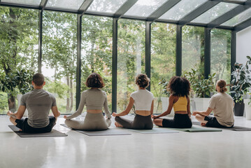 People meditating near panoramic windows with forest view 