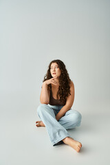 attractive plus size young girl in brown bra and blue jeans sitting and touching finger to chin