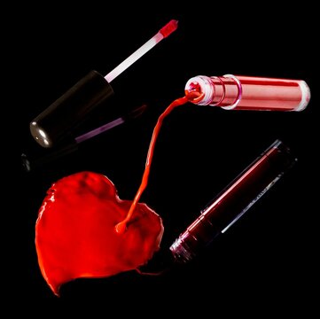 Ripe red lipstick spilling towards a dark surface creating a heart shape