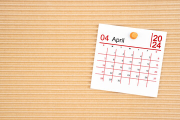 April 2024 calendar page with push pin on brown cardboard.
