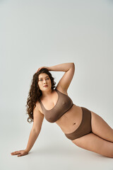 alluring plus size woman in lingerie with curly brown hair leaning on arm and putting hand on head - 768800726