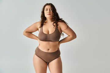 attractive plus size young woman in underwear with brown hair posing with hands on grey background