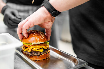 A chef’s hands meticulously assemble a juicy burger with fresh lettuce, melted cheese, and a glossy bun in a professional kitchen
